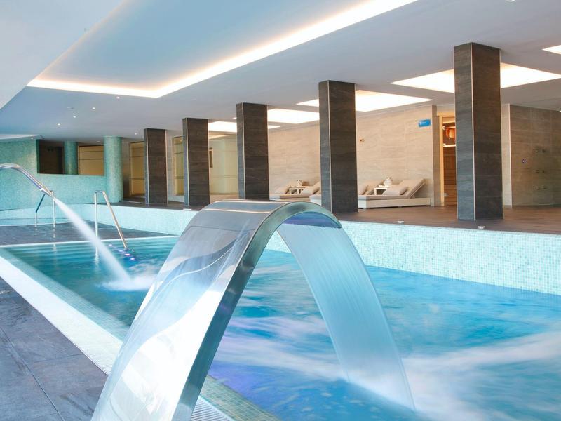 Piscine intérieure moderne avec jets d'eau, chaises longues et design élégant.