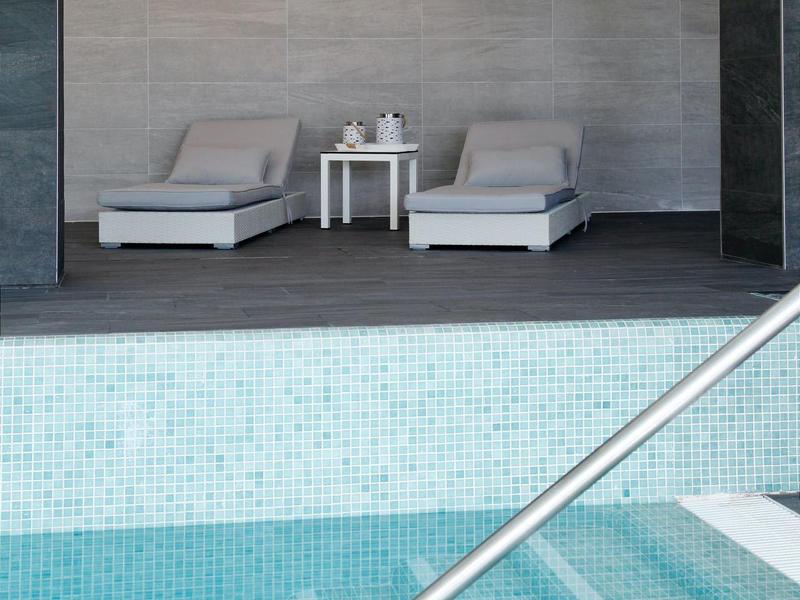 Nowoczesny basen z schodkami i dwoma szarymi leżakami obok małego stolika w pomieszczeniu.