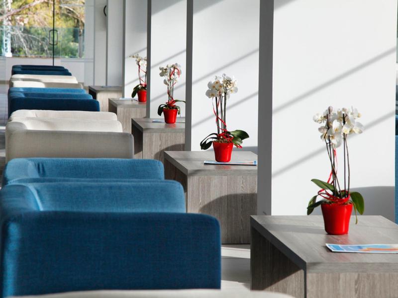 Fauteuils modernes et tables dans un hall d'hôtel lumineux avec orchidées en pot.