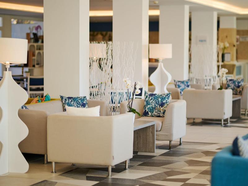 Hell eingerichteter Hotelraum mit weißen Sesseln, modernen Lampen und gemusterten Kissen
