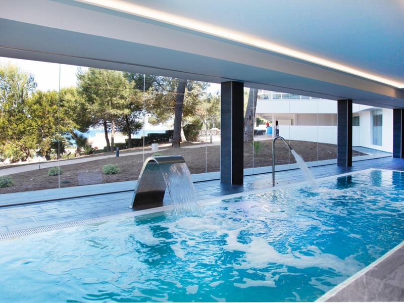 Piscine intérieure avec jets d'eau et grandes fenêtres donnant sur des arbres et de l'eau.