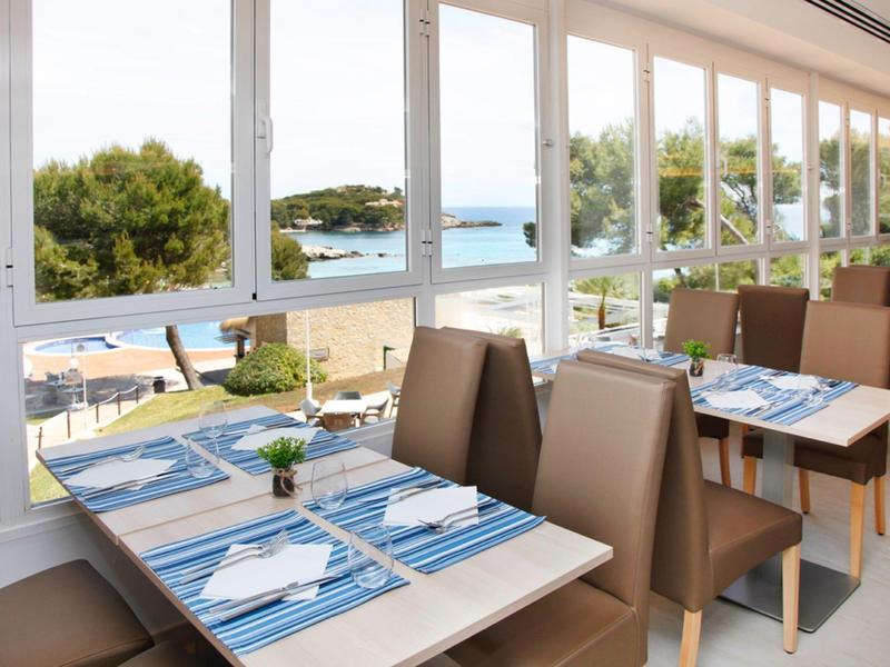 Restaurant lumineux avec vue sur la mer et tables dressées avec des sets bleus rayés.
