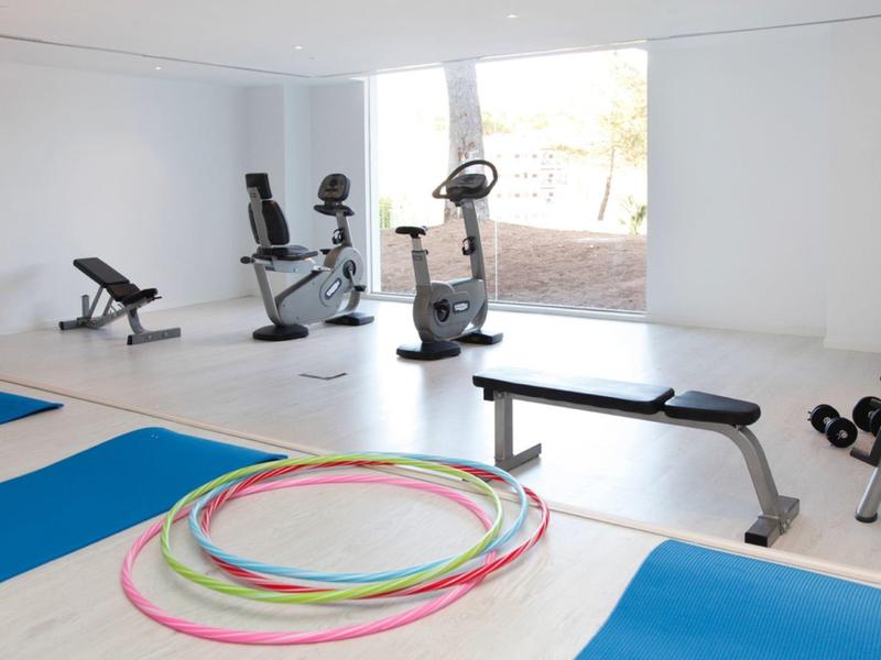 Salle de sport lumineuse avec vélos d'appartement, bancs, tapis et cerceaux colorés.