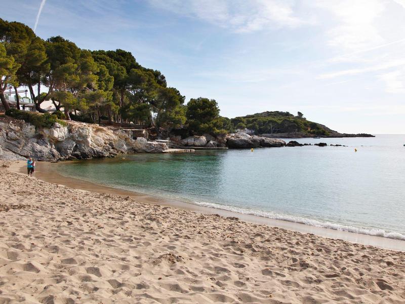 Plage de sable avec eau turquoise claire et côte rocheuse sous un ciel bleu.