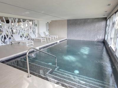 Moderní vnitřní bazén s lehátky a velkým postranním oknem.