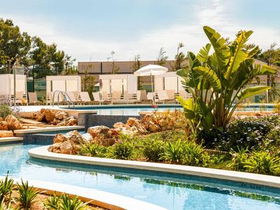 Pool mit Liegestühlen, Sonnenschirmen und tropischer Bepflanzung im Hotelgarten.