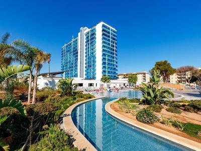 Moderní hotel s bazénem a palmami pod jasnou modrou oblohou