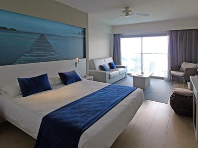 Helles Hotelzimmer mit Doppelbett, Sitzecke und großem Fenster mit Vorhängen.