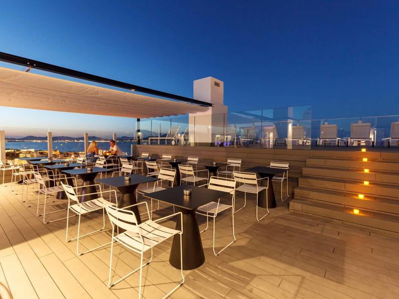 Moderní hotelová terasa s stolky, židlemi a osvětlením schodů při soumraku.