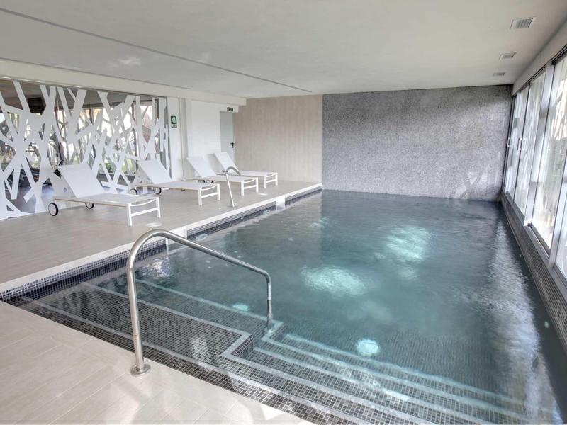 Moderní vnitřní bazén s lehátky a velkým postranním oknem.
