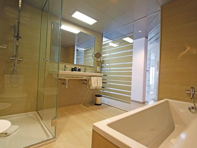 Světlá koupelna s vanou, skleněným sprchovým koutem a moderním zařízením.