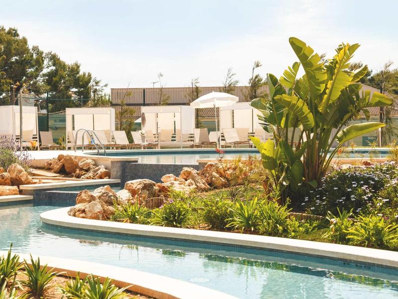 Moderní venkovní bazén s lehátky, slunečníky a zelenými rostlinami.