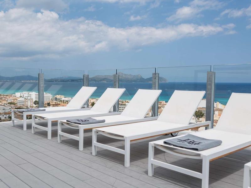 Bílé lehátka na dřevěné terase s výhledem na moře a zataženou oblohou.