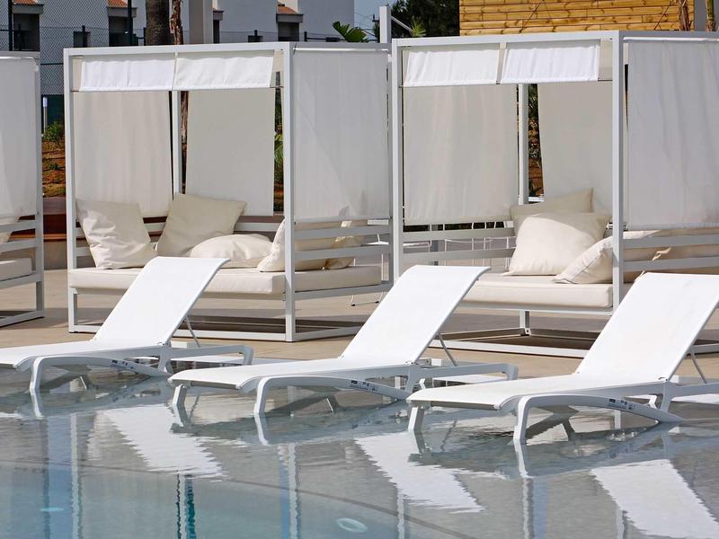 Bílé lehátka a kryté denní postele u bazénu za denního světla.