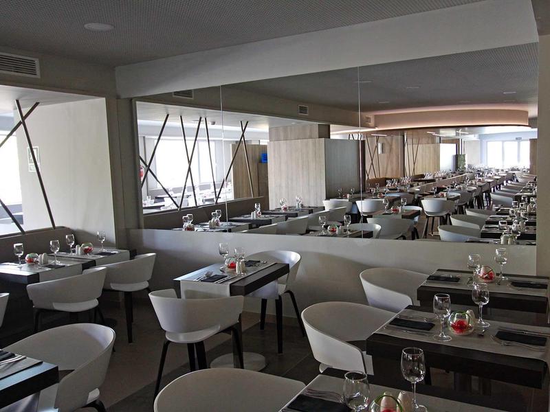 Velká moderní jídelna s bílými židlemi a prostřenými stoly.