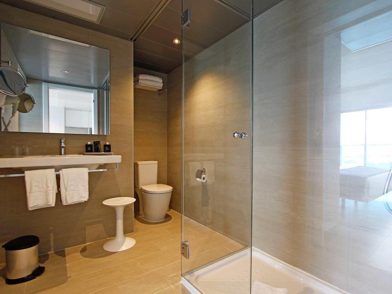 Moderní koupelna se skleněným sprchovým koutem, toaletou, umyvadlem a bílými ručníky.