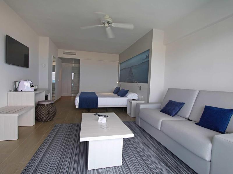 Moderně zařízený hotelový pokoj s pohovkou, posezením a televizí na zdi.