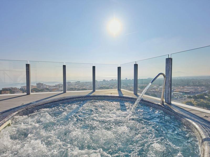 Blubbernder Whirlpool auf einer Dachterrasse mit Blick auf die Stadt bei sonnigem Himmel.