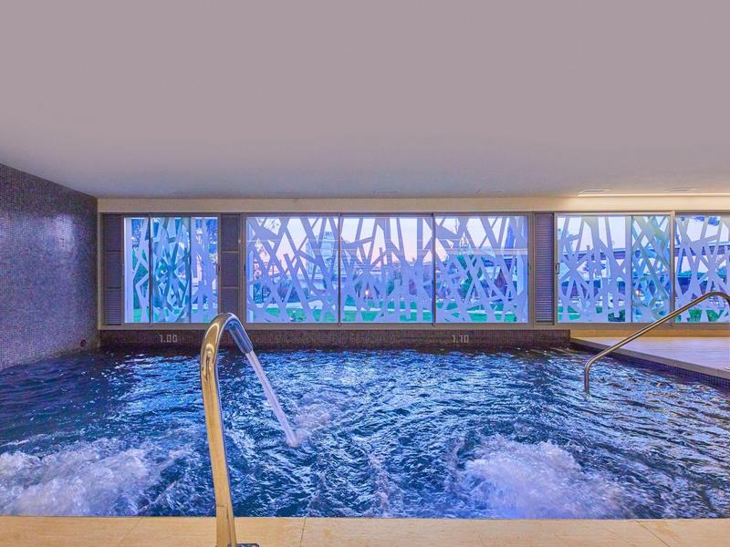 Innenpool mit Wasserfall-Funktion und dekorativen Fenstern in einem modernen Spa-Bereich.