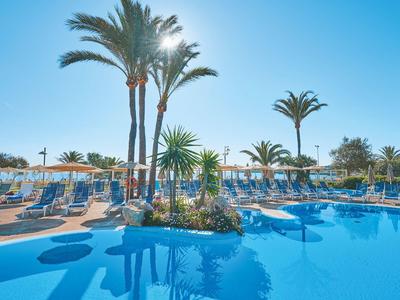 Sonnendurchfluteter Poolbereich mit Palmen und Sonnenliegen in einem Hotel.