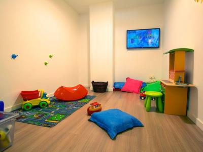 Heller Spielraum mit bunten Kissen, Spielzeug und einer Wandmontierten Fernseher.