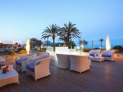 Außenbereich mit weißen Sitzmöbeln und Palmen mit Blick aufs Meer bei Dämmerung.