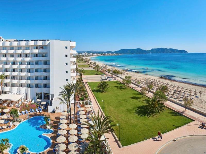 Großes Hotel mit Pool und Blick auf Strand und Meer bei sonnigem Wetter.