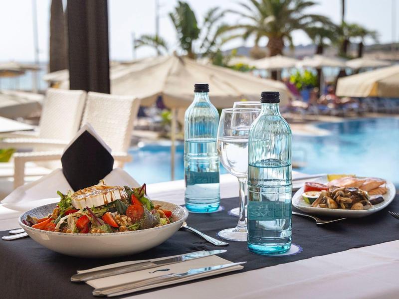 Frischer Salat und Getränke auf einem Tisch am Hotelpool im Freien.