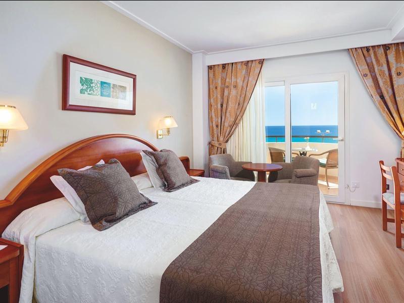 Helles Hotelzimmer mit Doppelbett, Meerblick und Balkon.