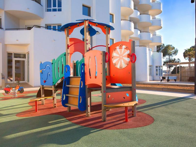 Bunter Spielplatz mit Klettergerüst und Rutsche vor modernen Wohngebäuden.
