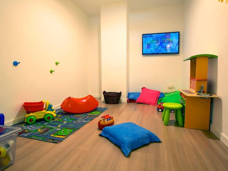 Heller Spielraum mit bunten Kissen, Spielzeug und einer Wandmontierten Fernseher.