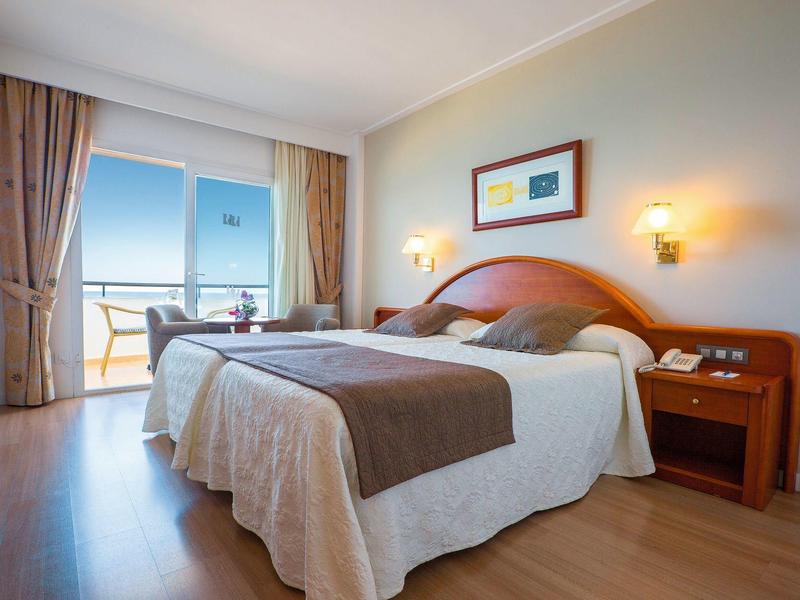 Gemütliches Hotelzimmer mit Doppelbett und Balkon mit Meerblick.