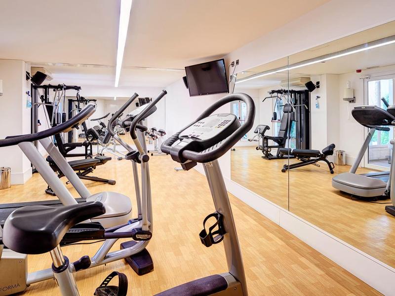 Moderner Fitnessraum mit Cardiogeräten und großen Spiegeln an den Wänden.