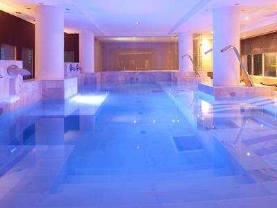 Piscine intérieure moderne avec éclairage bleu, colonnes et transats dans un hôtel.