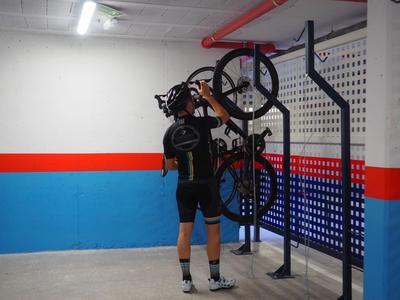 Mann steht in Fahrradkleidung in einer Garage und hebt ein Fahrrad an eine Wandhalterung.