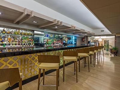 Espace bar d'hôtel moderne avec sol en bois, tabourets hauts et mur de bouteilles bien approvisionné.