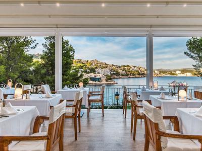 Restaurant élégant avec des tables blanches et vue sur une ville côtière au bord de la mer.
