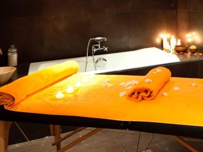 Un espace spa éclairé avec une table de massage et une baignoire en arrière-plan.