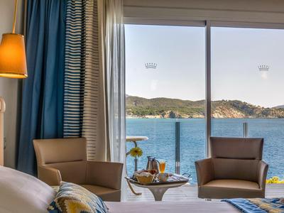 Chambre d'hôtel avec vue sur la mer, deux fauteuils et une petite table avec boissons près de la fenêtre