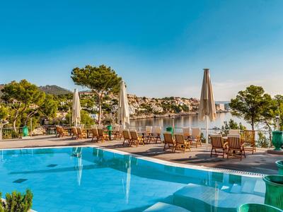 Vue sur une piscine extérieure avec chaises longues et parasols devant un lac en paysage ensoleillé.