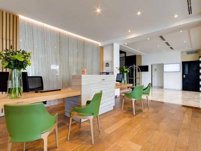 Hall d'accueil moderne avec sol en bois, murs blancs et chaises vertes.