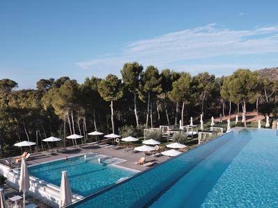 Deux piscines avec parasols et arbres en arrière-plan sous un ciel bleu.