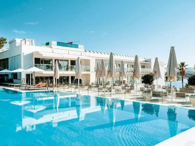 Hôtel moderne avec grande piscine extérieure, parasols et espaces de détente sous un ciel clair