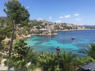 Vue sur une mer bleue claire avec village côtier, arbres verts et bateaux par temps ensoleillé.