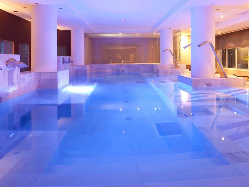 Piscine intérieure moderne avec éclairage bleu, colonnes et transats dans un hôtel.