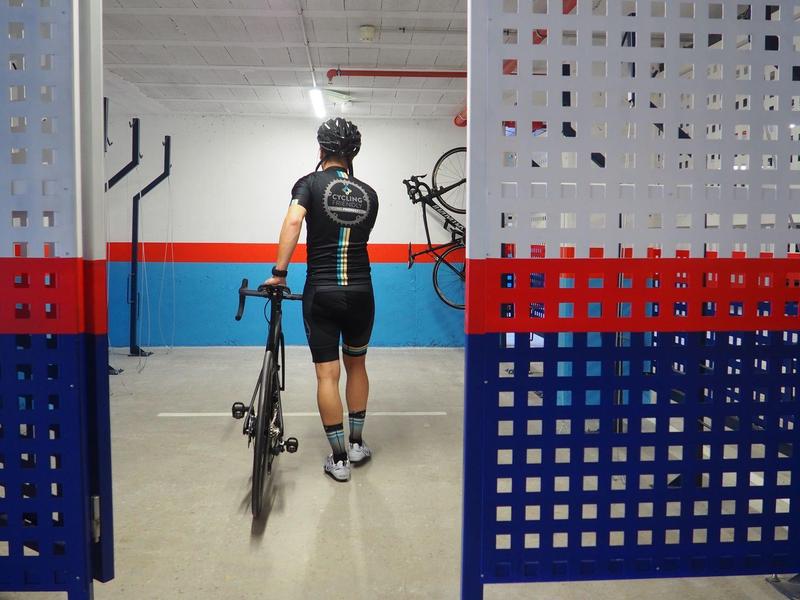 Cycliste en tenue sportive tenant son vélo de route dans un garage coloré aux murs bleu et rouge.