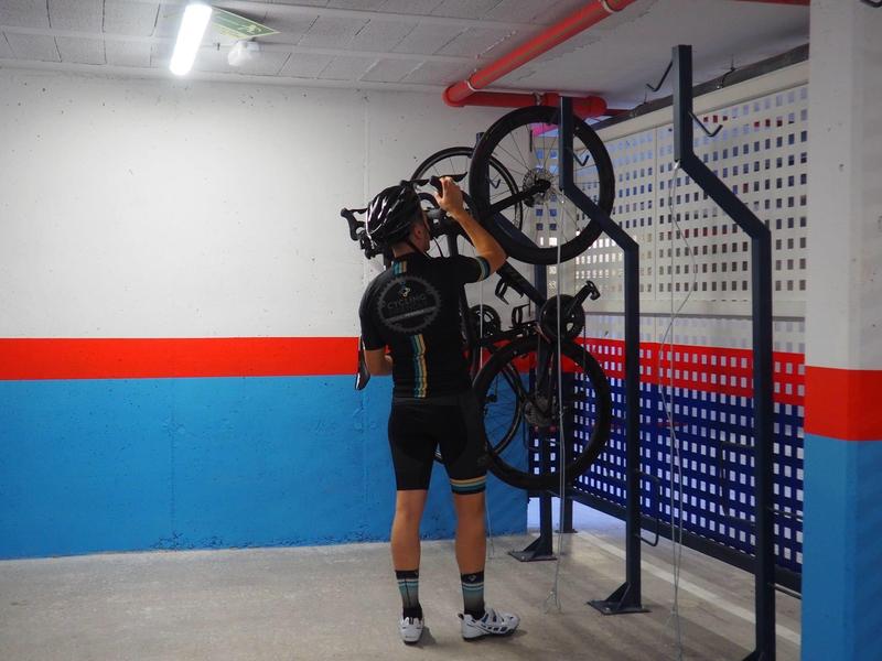 Cycliste en tenue de sport levant un vélo dans un garage souterrain aux murs bleus et rouges.