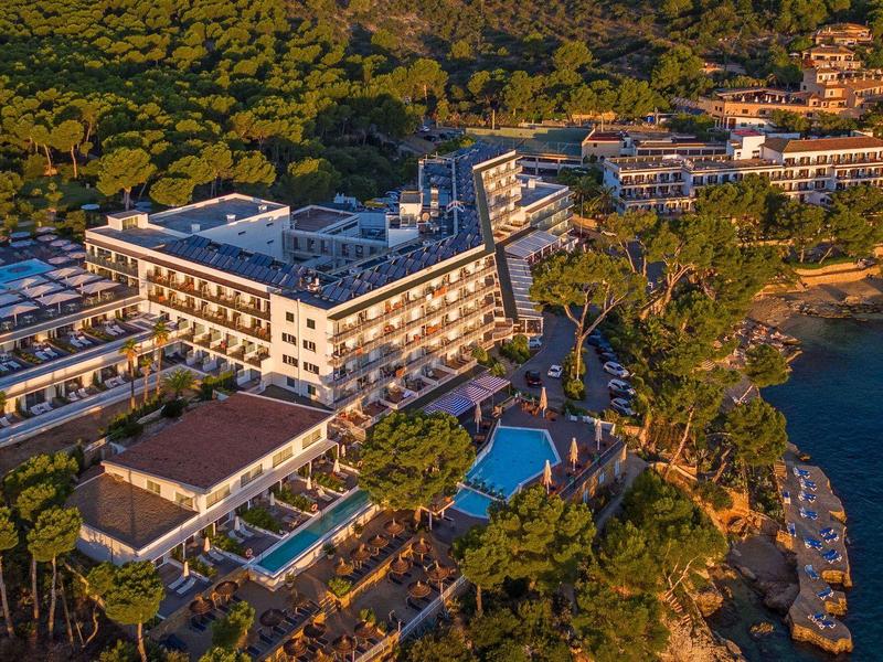 Photo aérienne d'un complexe hôtelier avec piscine et accès direct à la mer dans une région côtière boisée.
