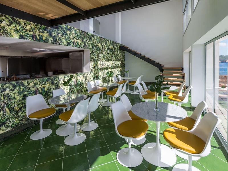 Espace extérieur moderne avec tables blanches et chaises jaunes, vue sur la mer.