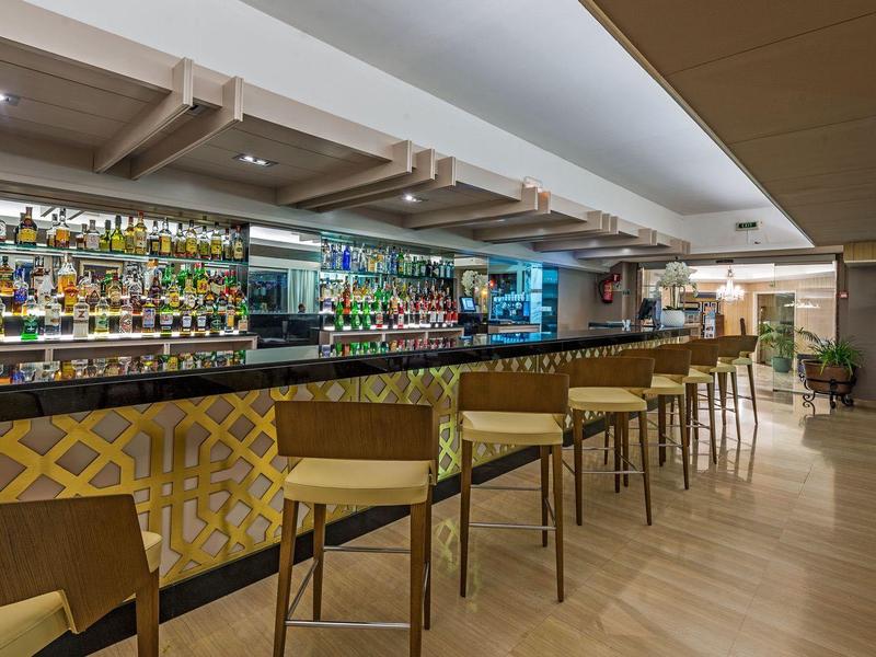 Espace bar d'hôtel moderne avec sol en bois, tabourets hauts et mur de bouteilles bien approvisionné.